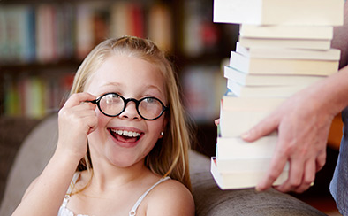 Person bringing a large stack of books to a smiling child