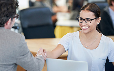 Smiling woman reaching across desk to shake hands with a man