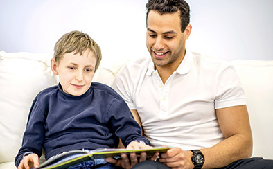 A child and an adult sitting next to each other on a couch while the child reads a braille book